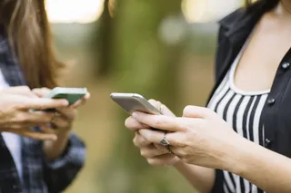 Dois celulares em primeiro plano, na mão de duas mulheres