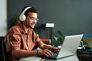 Homem vestindo marrom utiliza notebook e headphone branco