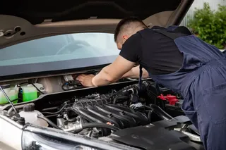 Mecánico revisando el motor de un auto compacto en un taller certificado.