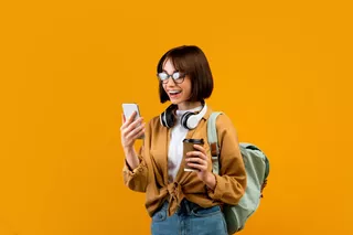 Mujer joven sonriente tomando un café mientras chequea su celular