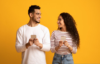 Hombre y mujer sonrientes mientras utilizan sus celulares