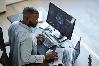 Homem utiliza notebook e PC para realizar trabalho