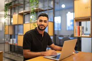 Homem sorri enquanto utiliza notebook em um escritório