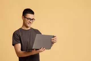 Un hombre joven sonríe al usar su MacBook de Apple