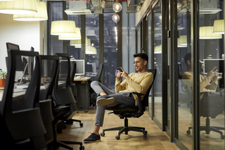 Homem mexe em telefone celular enquanto está sentando em uma cadeira de escritório