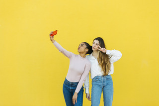 Dos mujeres tomándose una selfie en fondo amarillo