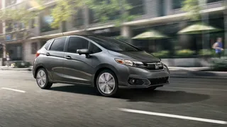 Automóvil Honda Fit gris con fondo urbano en movimiento