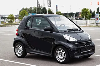 Auto compacto Smart negro circulando junto a pared clara en calle