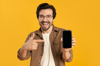 Homem aponta para um smartphone em um fundo amarelo.