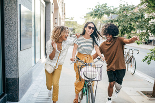 Mulher anda de bicicleta estilo passeio ao lado de dois amigos, em uma calçada