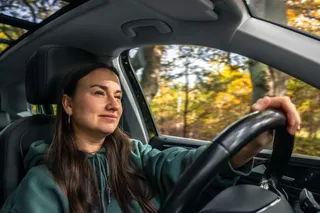 Persona sonriente al volante de una SUV compacta en carretera.