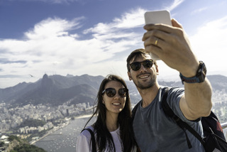 Casal tira selfie no alto de uma montanha.