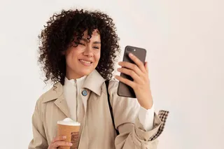 Mulher com café na mão usando smartphone
