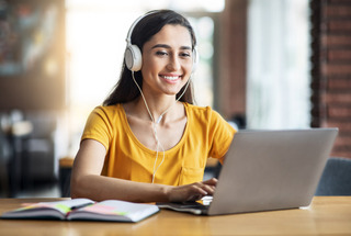 Una chica joven sonríe mientras hace un trabajo práctico de la universidad en su computadora Dell