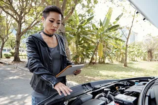 Mujer revisa motor del auto con capó abierto