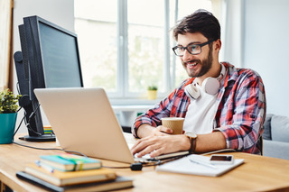 Un hombre joven usa su laptop y PC para trabajar en su hogar