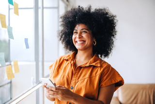 Mulher sorri enquanto segura um smartphone.