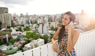 Mujer joven utiliza su celular en la terraza de un edificio