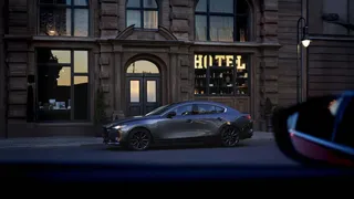 Mazda 3 negro junto a la acera frente a un hotel