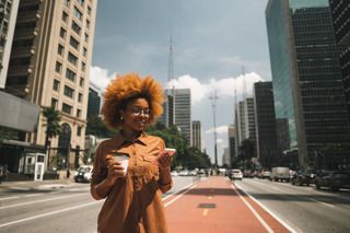 Mulher vestindo roupa marrom, usa o smartphone no meio de uma avenida