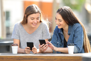 Dos mujeres comparan sus teléfonos móviles mientras beben café