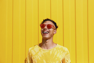 Homem com camisa amarela sorri, enquanto usa óculos de sol.