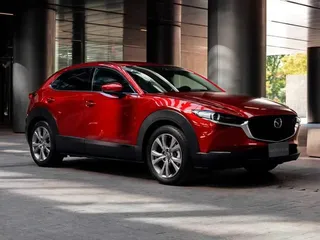 Automóvil Mazda CX-30 rojo estacionado frente a modernos edificios urbanos.