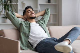 Un hombre se relaja en un sofá mientras escucha música en sus auriculares inalámbricos