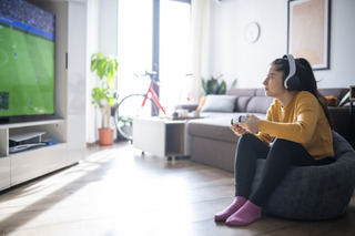 Mulher joga videogame no sofá da sala