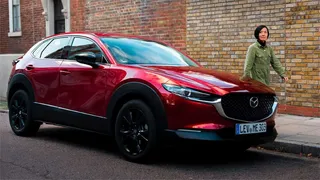 Vista lateral de una Mazda CX-30 en color rojo Soul Red Crystal estacionada en una calle urbana, mostrando su diseño compacto y líneas de carrocería características del modelo.