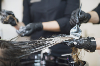 Cabeleireira descolorindo o cabelo de uma cliente.