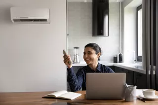Una mujer prende el aire acondicionado para ventilar el ambiente mientras usa su notebook