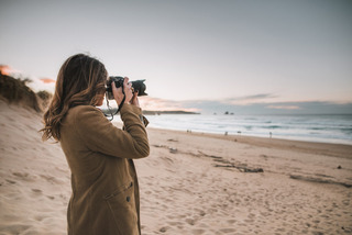 Mujer sacando foto con su cámara réflex al atardecer en una playa