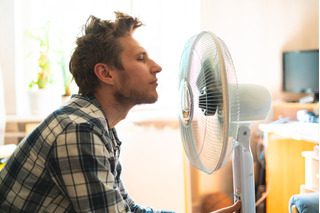 Hombre acalorado refrescándose con un ventilador