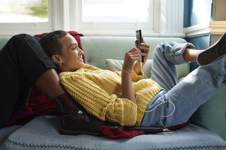 Mulher se distrai usando um celular no sofá