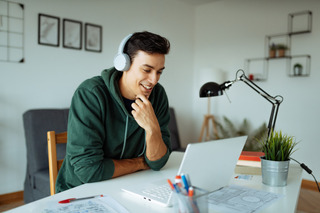 Homem utiliza notebook em uma mesa branca.