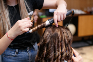 mulher cacheando cabelos com babyliss em salão, feito por outra mulher