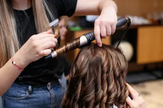 mulher cacheando cabelos com babyliss em salĂŁo, feito por outra mulher