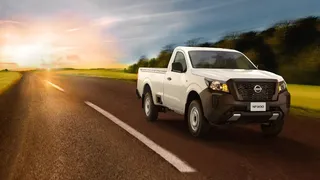 Camioneta Nissan NP300 blanca conduciendo por carretera al atardecer en campo abierto.