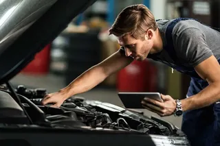 Persona revisando el motor de un auto compacto en un taller mecánico.
