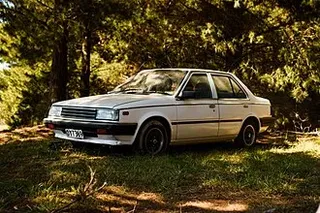 Nissan Tsuru blanco estacionado en un bosque de México, vista lateral completa del vehículo.