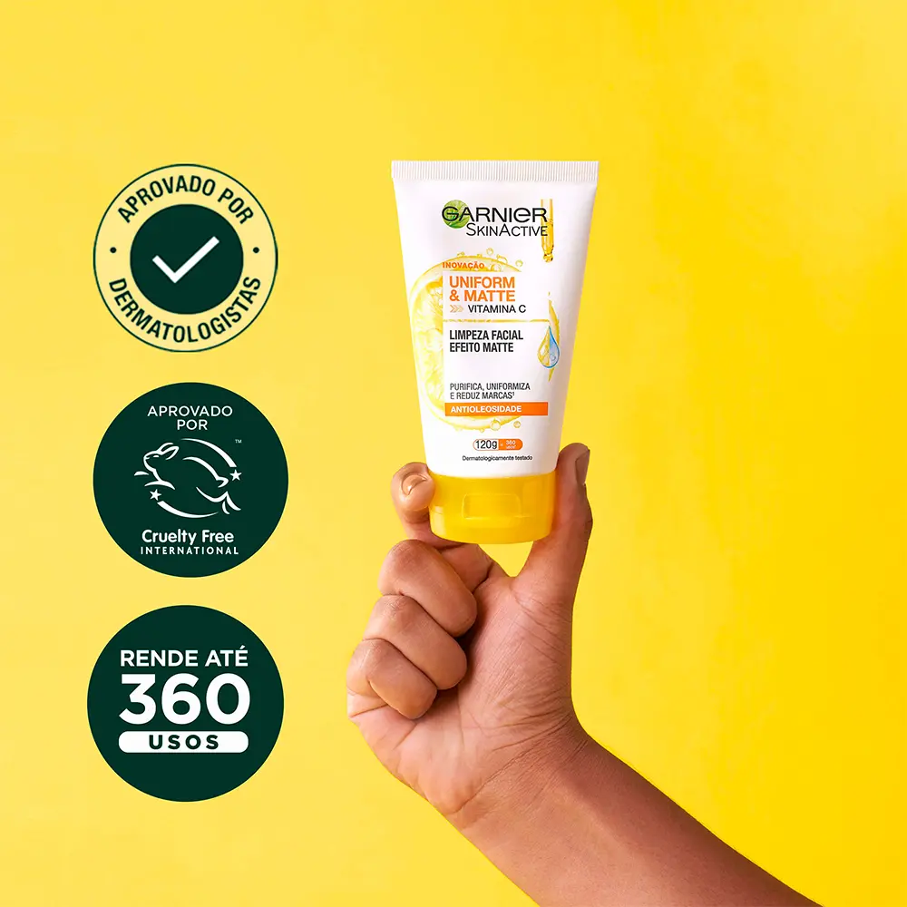 Mão segurando o tubo do limpador facial Garnier com ícones de aprovação dermatológica, selo Cruelty Free e rendimento de 360 usos.