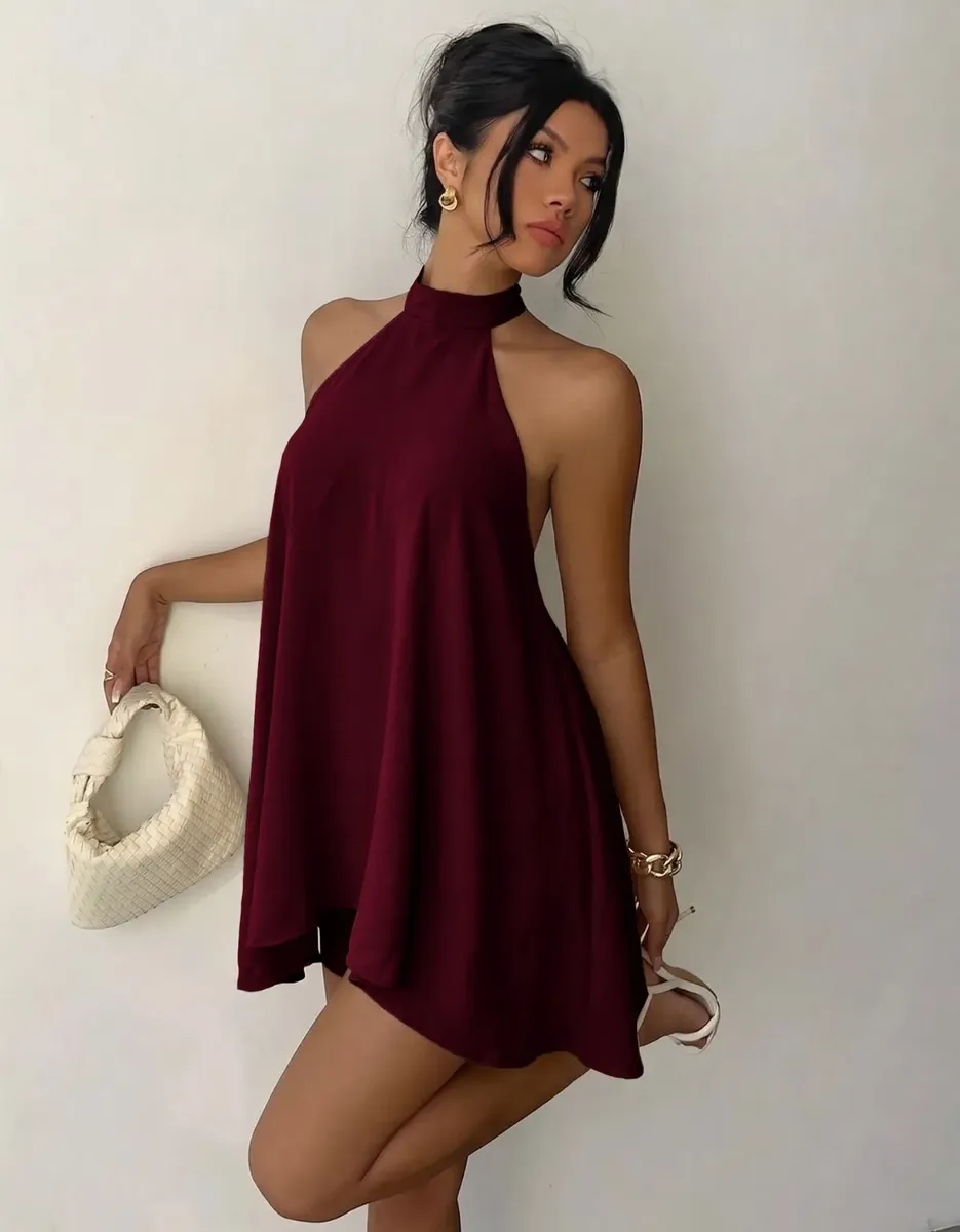 Modelo de perfil posando com bolsa clara, destacando o modelo frente única do vestido vinho.
