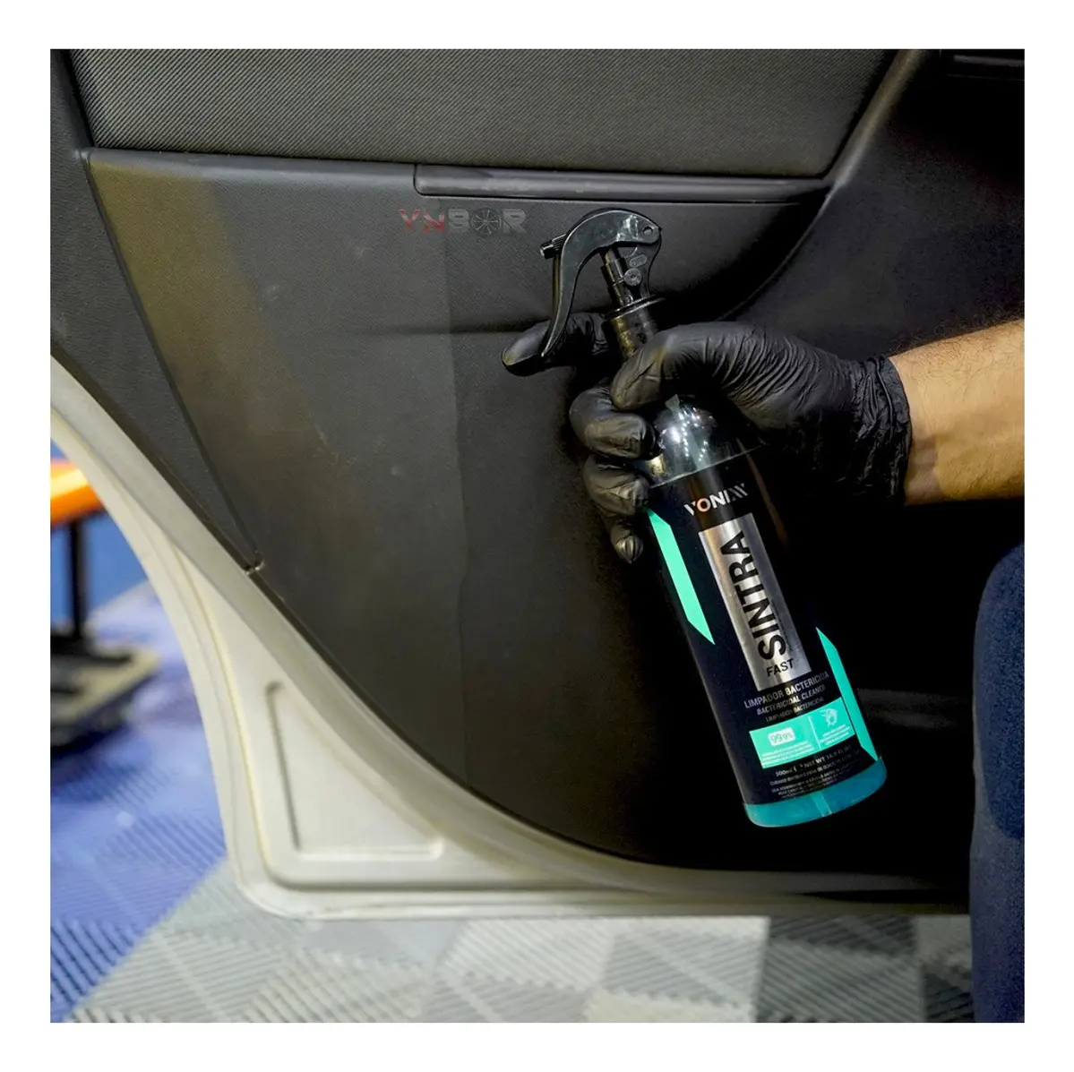 Mão com luva preta segurando um frasco do produto SINTRA FAST da Vonix, aplicando no painel de uma porta de carro com resultado visível de limpeza.