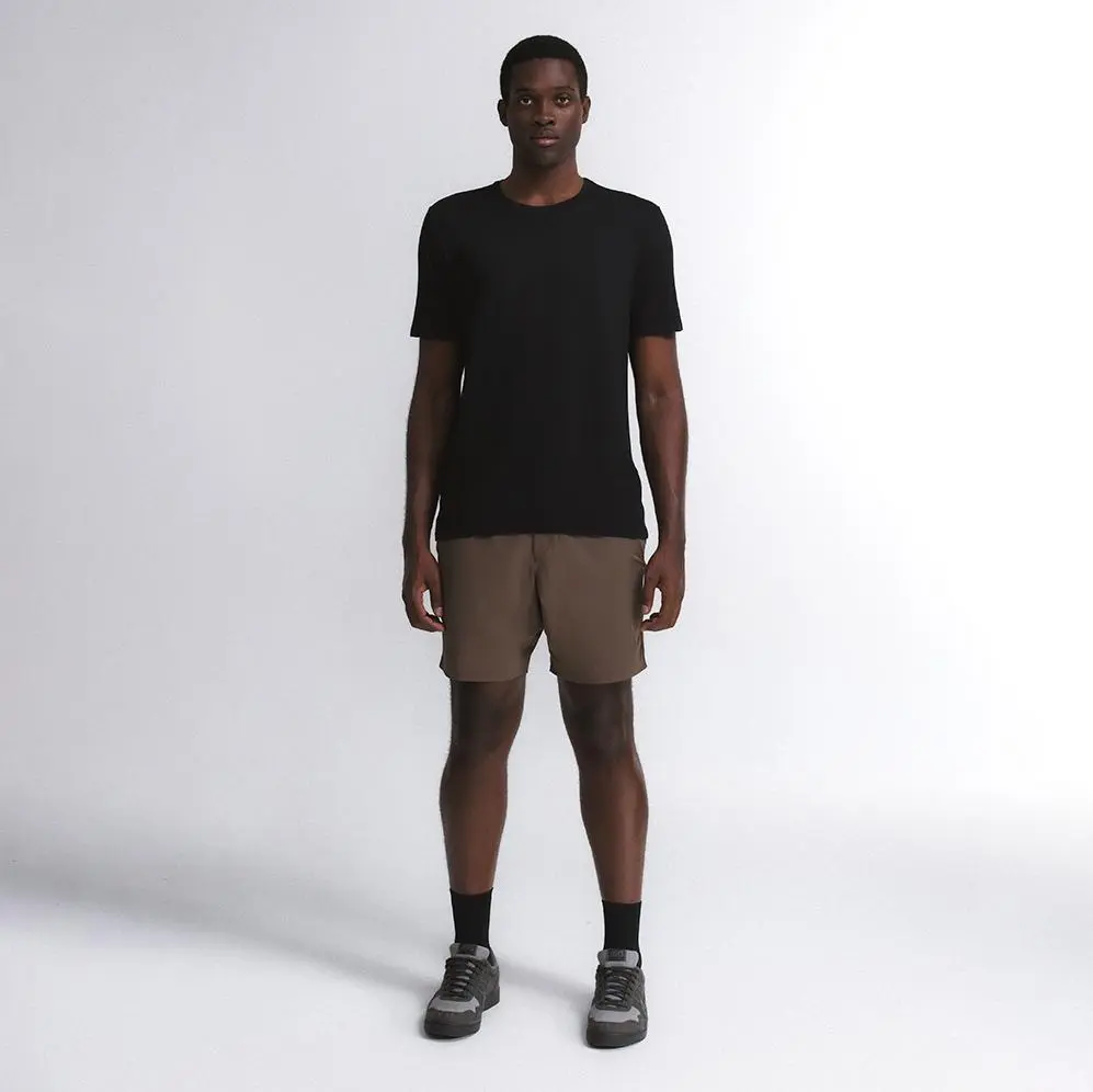 Homem em corpo inteiro vestindo camiseta preta e bermuda marrom