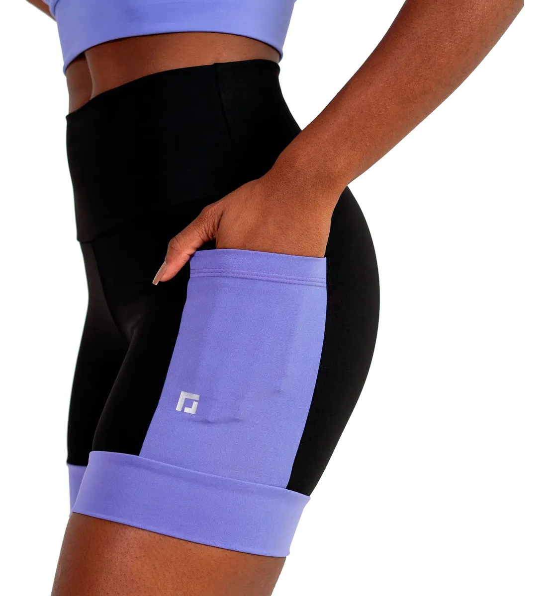 Close-up da mão de uma mulher colocando um celular em um bolso lateral de shorts pretos com detalhes roxos