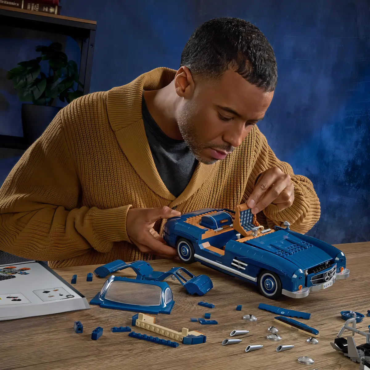 Pessoa montando as peças do carro Mercedes-Benz 300 SL em uma mesa de madeira