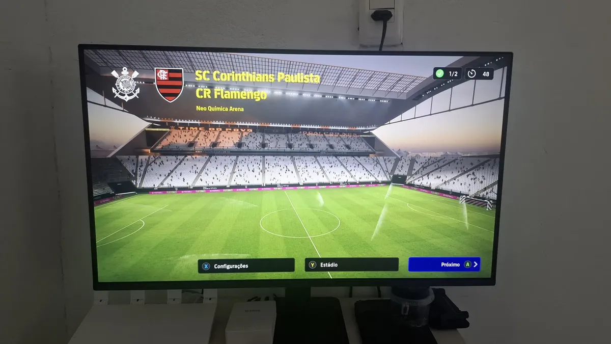 Monitor LG exibindo a tela inicial de um jogo de futebol com estádios e times.