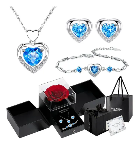 Conjunto de joias feminino com colar, brincos e pulseira em formato de coração azul, exibido com uma rosa preservada e caixas de presente.