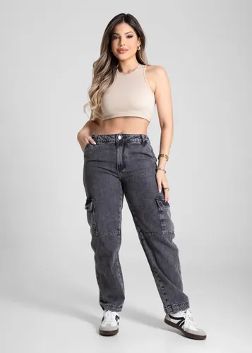 Mulher usando calça jeans preta barrel e top bege, em pé de frente para a câmera.